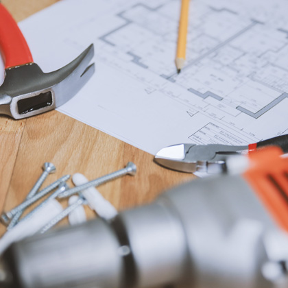 A table with a blueprint, pencil, hammer, screws, snippers, and a drill