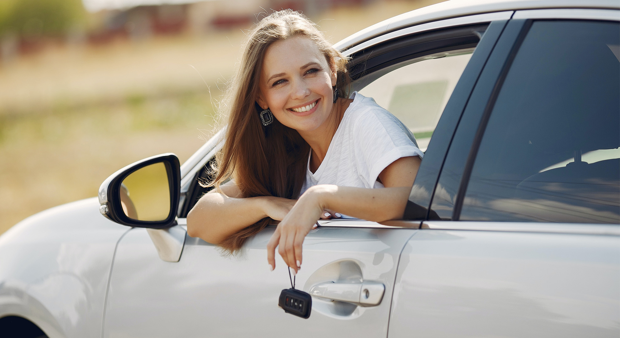 Woman hanging out of car window holding keys and smiling