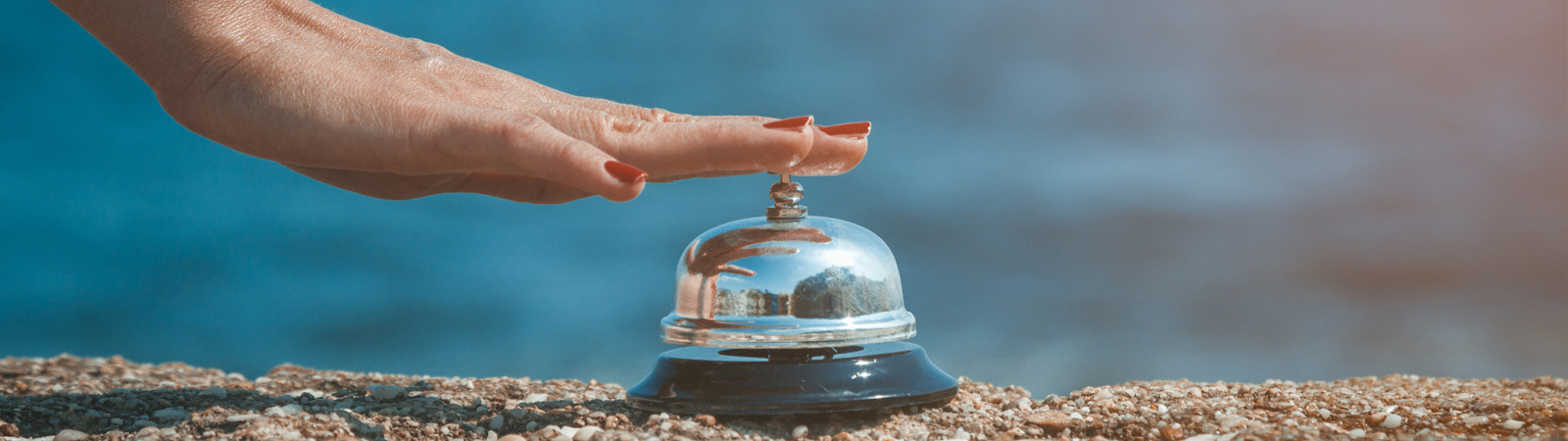 A woman pressing the button of a butler's bell on a rocky beach with the ocean in the background