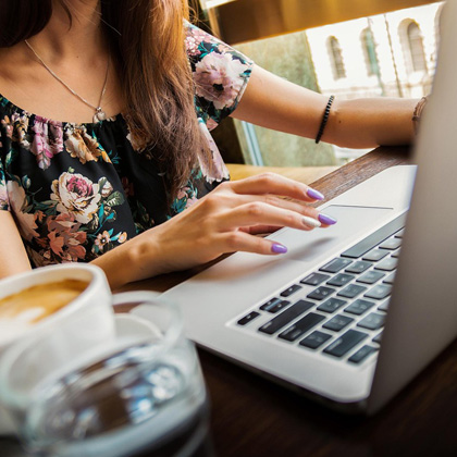 Woman at a table using a laptop with a coffee nearby